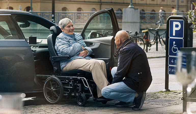 Ein Mann hilft einer Frau, die in einem Carony sitzt, ins Auto