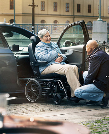 Man assissting woman in a wheelchair car seat transferring into a car from a Carony