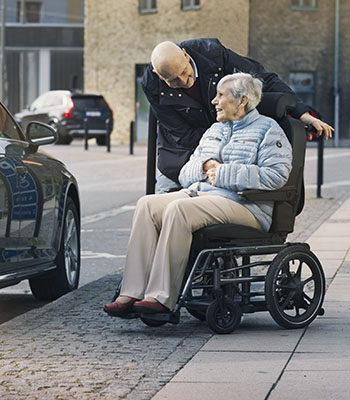 Man standing slightly behind woman on wheelchair and smiling  at her 