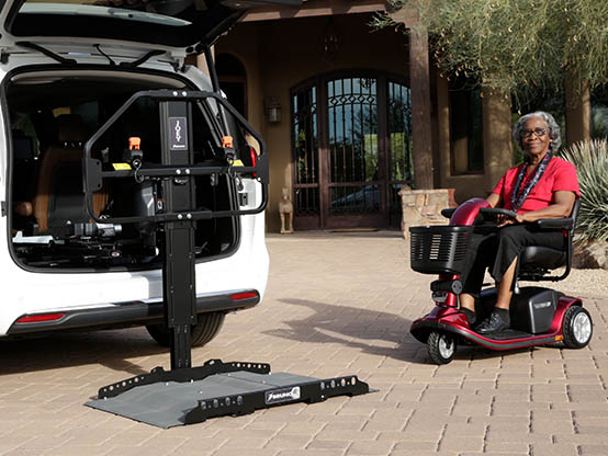 Frau, die ihren elektrischen Rollstuhl auf einen in einem Auto installierten Joey Lift fährt