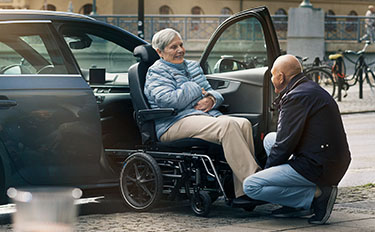 Picture of a man assisting a woman on a wheelchair into a car with the help of a Carony